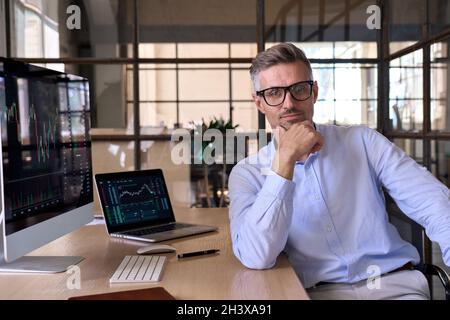 Serious männlich ceo Geschäftsmann Händler Blick auf Kamera am Schreibtisch mit pc-Computern. Stockfoto