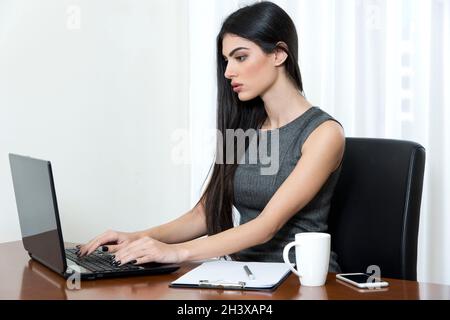 Junge Geschäftsfrau, die in ihrem Büro sitzt und auf ihrem Laptop tippt. Stockfoto