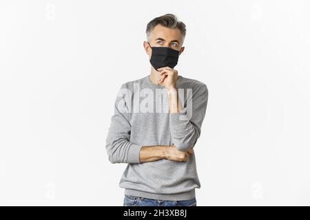 Covid-19, Pandemie und soziales Distanzierungskonzept. Porträt eines nachdenklichen Mannes mittleren Alters, der die Entscheidung trifft, mit medizinischer Maske, Stockfoto