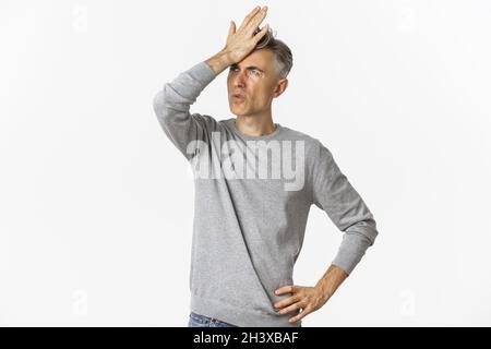 Bild von frustrierten und notleidenden Mann mittleren Alters, Facepalm und Ausatmen enttäuscht, stehend über weißem Hintergrund Stockfoto