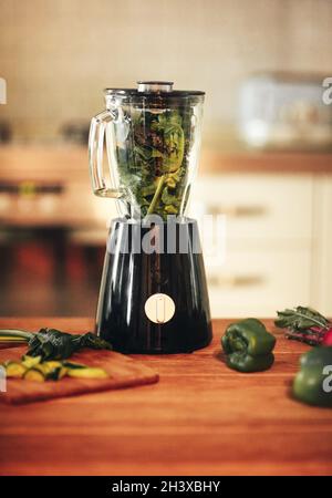 Smoothie-Mixer mit grünem Gemüse in der Küche mit Grünblättrig im Inneren Stockfoto