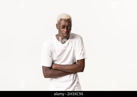 Porträt eines kranken afroamerikanischen blonden Mannes, der sich vor Magenschmerzen beugt, starke Schmerzen hat, vergiftetes Essen hat und über Weiß steht Stockfoto