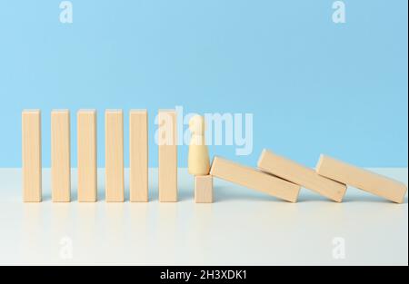 Figuren von Männern halten das Fallen von Holzblöcken zurück, die Wirkung von Dominos auf blauem Hintergrund. Konzept der Teamarbeit Stockfoto