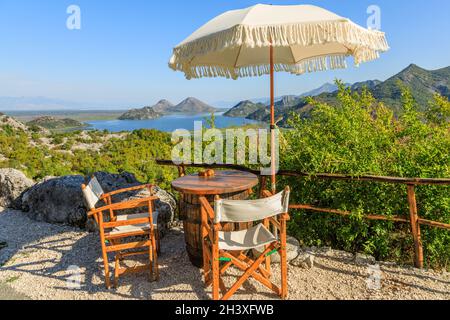 Panoramablick auf den Skadar See und die Berge vom Straßencafé mit Tischen, Stühlen und Sonnenschirmen, Montenegro Stockfoto