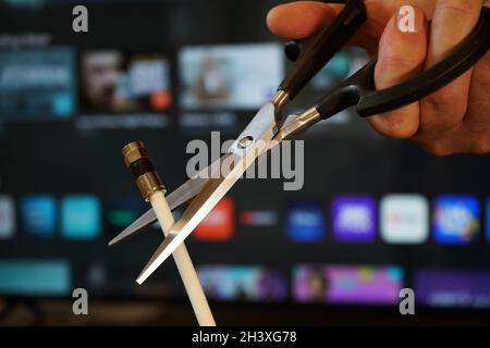 Schere schneidet durch ein Koaxialkabel mit TV-Fokus im Hintergrund - schneiden Kabel-tv-Konzept Stockfoto