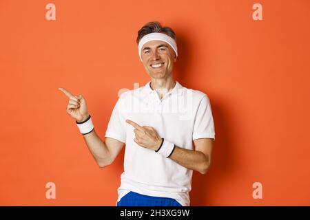 Porträt eines aktiven und gesunden Mannes, der Sport macht, aktiv trägt, lächelt und mit den Fingern auf die Promo-Workout zeigt, steht Stockfoto