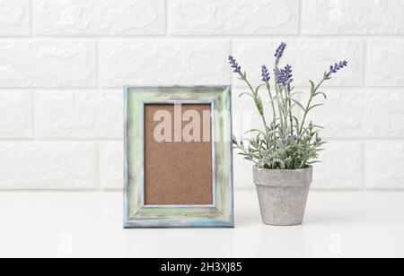 Leerer weißer Bilderrahmen aus Holz und Blumentöpfe mit Pflanzen auf weißem Tisch Stockfoto