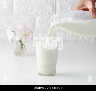 Prozess des Gießen von frischer Milch aus einer Plastikflasche in eine Glastasse, weißen Tisch Stockfoto