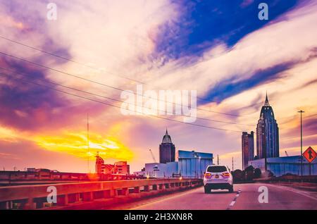 Die Sonne geht über der City of Mobile unter, während der Verkehr der Interstate 10 auf der Mobile Bayway am 23. Oktober 2021 in Mobile, Alabama, nach Westen fährt. Stockfoto