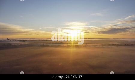 Morgennebel, Sonnenstrahlen und lange Schatten im Nebel, der sich zwischen den Bäumen im Tal in der Nähe des Dorfes erstreckte Stockfoto