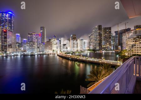 Die Skyline von Miami in der Nacht leuchtet und leuchtet, wie man sie von der anderen Flussseite aus am Einlass am Ende einer Halbinsel mit dem bewölkten Himmel nach dem Regen sieht Stockfoto