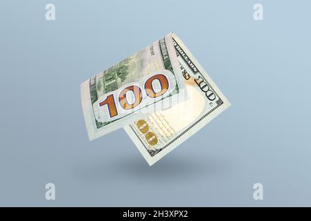 Ein gebogener 100-Dollar-Schein fällt im freien Fall und wirft einen Schatten auf einen blauen Hintergrund, eine Stgflation oder ein Inflationskonzept. Stockfoto