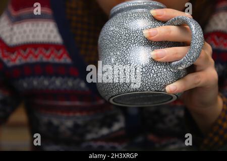 Nahaufnahme der weiblichen Hände mit einem Becher Getränk. Junge Hipster-Frau im Weihnachtspullover mit einer Tasse Tee oder Kaffee. Gemütliches warmes Keramikgetränk. Lang n Stockfoto