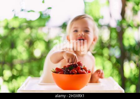 Lächelndes Kind greift in der Schüssel auf dem Tisch nach Früchten Stockfoto