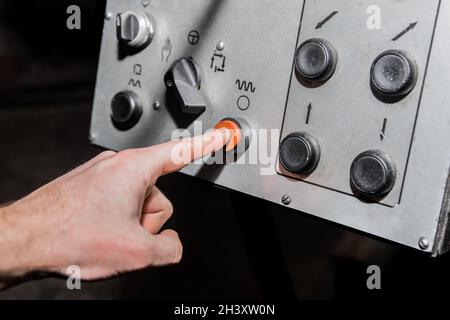 Die Hand des Arbeiters drückt mit dem Finger die rote Taste auf dem alten System und Bedienpult von Industrieanlagen. Stockfoto