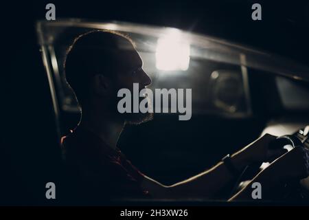 Man Fahrer sitzt am Lenkrad des Autos in der Nacht Stockfoto