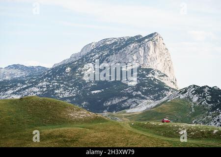 Zabljak, Montenegro - 23. juli 2020: Touristen in einem roten Auto, zelteten auf dem Gras, vor der Kulisse eines felsigen Berges in der Nähe von Th Stockfoto