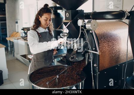 Kaffeekühlung in der Röstermaschine beim Rösten des Kaffees. Junge Angestellte Barista, die Kaffeebohnen mischt. Stockfoto