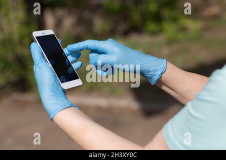 Der Mann hält das Mobiltelefon in medizinischen Handschuhen in den Händen Stockfoto