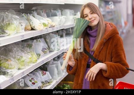 Junge Frau mit einem Lebensmittelkorb wählt Produkte in der Gemüseabteilung aus. Stockfoto