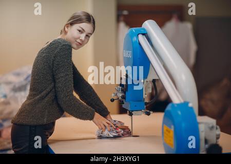 Junge schöne Schneiderin Kleidung Designer schneidet Stoff auf der Maschine Stockfoto