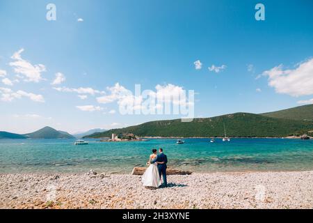 Braut und Bräutigam umarmen sich am Strand der Insel Mamula vor dem Hintergrund der alten Festung Stockfoto