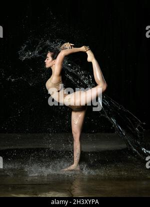 Junge schöne Frau mit kaukasischem Aussehen und langen Haaren tanzt in Wassertropfen auf schwarzem Hintergrund. Springen und Schwingen Stockfoto