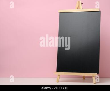 Leere schwarze Schiefertafel auf weißem Tisch, rosa Hintergrund. Platz für die Inschrift der Ankündigung Stockfoto