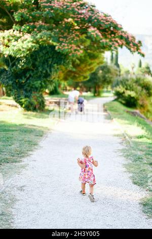 Kleines Mädchen, das den Schotterweg im grünen Park entlang läuft Stockfoto