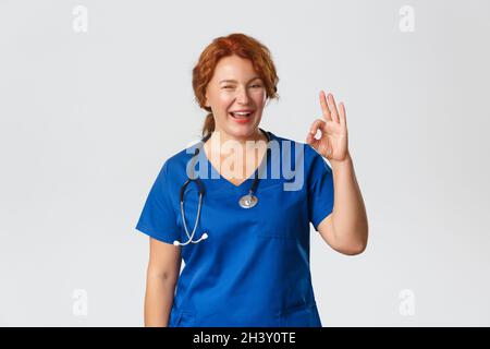 Medizin, Gesundheitswesen und Coronavirus-Konzept. Selbstbewusste professionelle Arzt versichern alles in Ordnung, fröhlich mittleren Alters Rotschopf Stockfoto