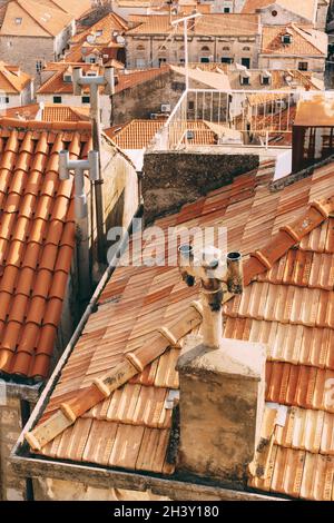 Alte orangefarbene Dächer mit rostigen Kaminen und einem Dachbalkon. Stockfoto