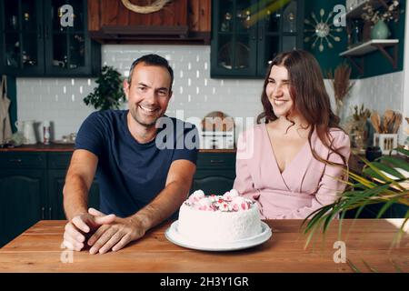 Mann und junge Frau sitzen in der heimischen Küche mit Kuchen auf dem Tisch Stockfoto