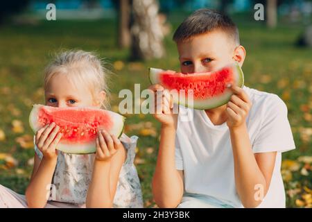 Um nette Kinder lttle Junge und Mädchen essen saftige Wassermelone Im Picknick auf der Herbstparkwiese Stockfoto