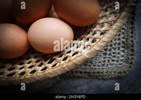 Blick von oben auf die Eier in einem Strohkorb auf einem natürlichen Stoffservietten und ein rustikales Holz- Hintergrund Stockfoto