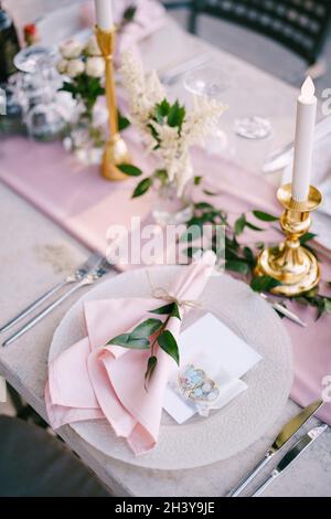 Hochzeitsessen Tischempfang. Steintisch mit rosa Läufer, Teller mit Muster und rosafarbene Servietten, Kerzen mit LED-Licht b Stockfoto