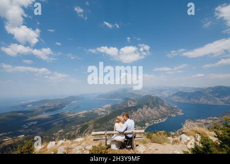Ein Mann und eine Frau sitzen in einer Umarmung auf einer Bank, vor ihnen öffnet sich ein Panoramablick auf die Bucht von Kotor Stockfoto