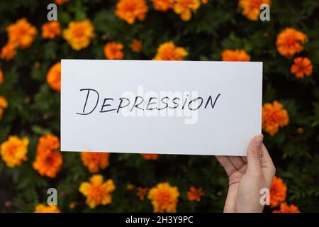 Frau hält in der Hand weißes Blatt Papier mit dem Wort Depression auf Blumenhintergrund Stockfoto
