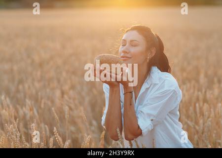 Frau hält hausgemachtes Weizenbrot in den Händen im Weizenfeld bei Sonnenuntergang. Stockfoto