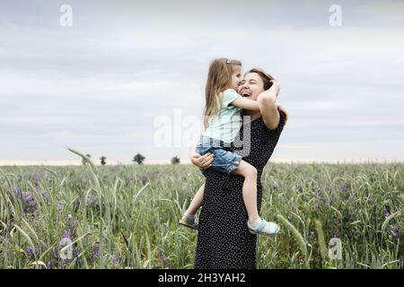 Glückliche Mutter und Tochter mit Blumenstrauß umarmt in grüner Wiese Stockfoto