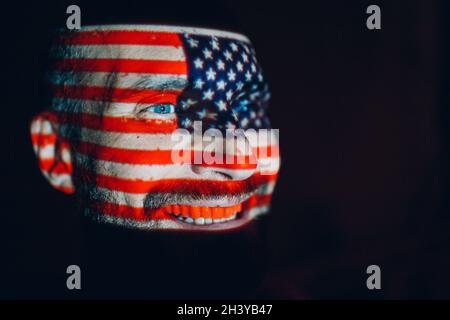 Erwachsener Mann mit USA-Flagge im Gesicht im Dunkeln. Stockfoto