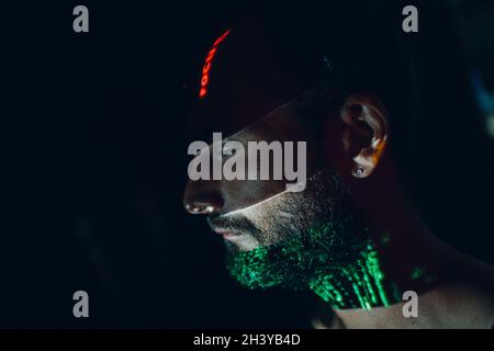 Junger Mann mit Buchstaben im Gesicht im Cyberpunk-Dunkel. Stockfoto