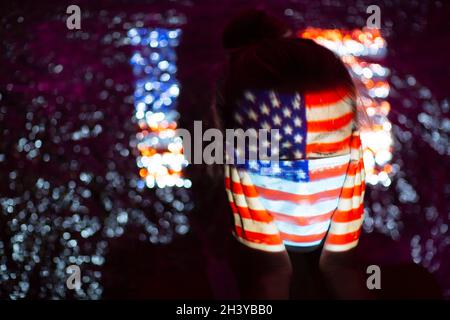 Junge Frau mit US-Flagge auf ihrem Gesicht in medizinischer Maske Stockfoto