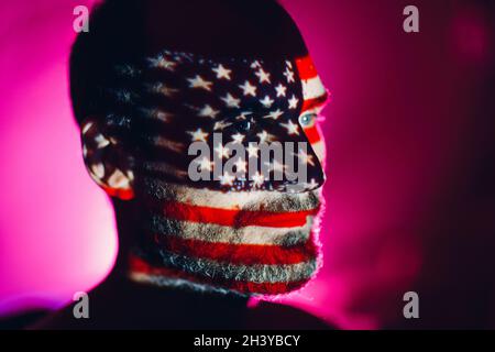 Erwachsener Mann mit USA-Flagge im Gesicht im Dunkeln. Stockfoto