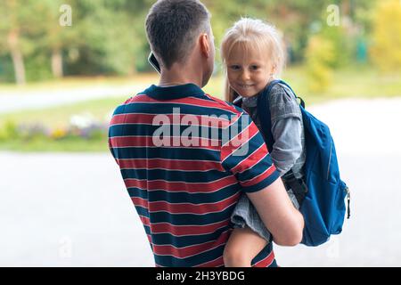 Rückansicht des Vaters, der mit ihm zurück zur Schule ging Tochter trägt Rucksack Stockfoto