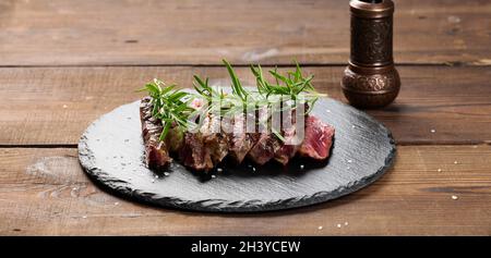 Gebratenes Stück Rindfleisch Ribeye in Stücke geschnitten auf einem schwarzen Brett, seltenes Maß an Donness. Köstliches Steak Stockfoto