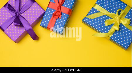 Geschenkbox mit Seidenband auf gelbem Hintergrund gebunden, Draufsicht. Festlicher Hintergrund Stockfoto