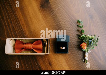 Accessoires für den Bräutigam Fliege, Gold Ehering und boutonniere auf einem Holzboden in einer Reihe. Stockfoto