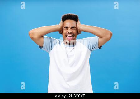 Überwältigend aus vielen Informationen. Porträt eines verzweifelten afroamerikanischen Studenten in T-Shirt mit Händen am Kopf Stockfoto