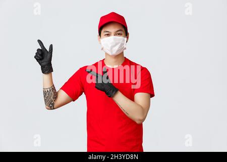 Freundlicher asiatischer Kurier in roter Uniform und Mütze, tragen Sie medizinische Schutzmaske und Handschuhe für die sichere Lieferung von Paketen an Ihren Porc Stockfoto