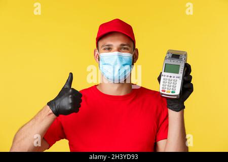 Covid-19, Lieferaufträge, Shopping, kontaktloses Bezahlen und soziales Distanzierungskonzept. Zufrieden schöner Kurier in rot unifor Stockfoto